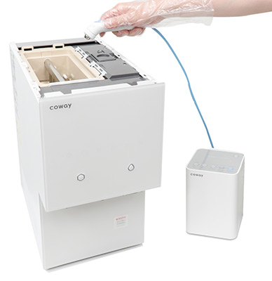 Gloved technician inserting a cleaning hose into an open Coway water purifier